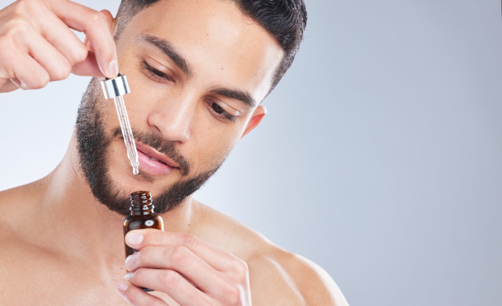 Studio shot of a handsome young man applying serum to his face against a grey background
