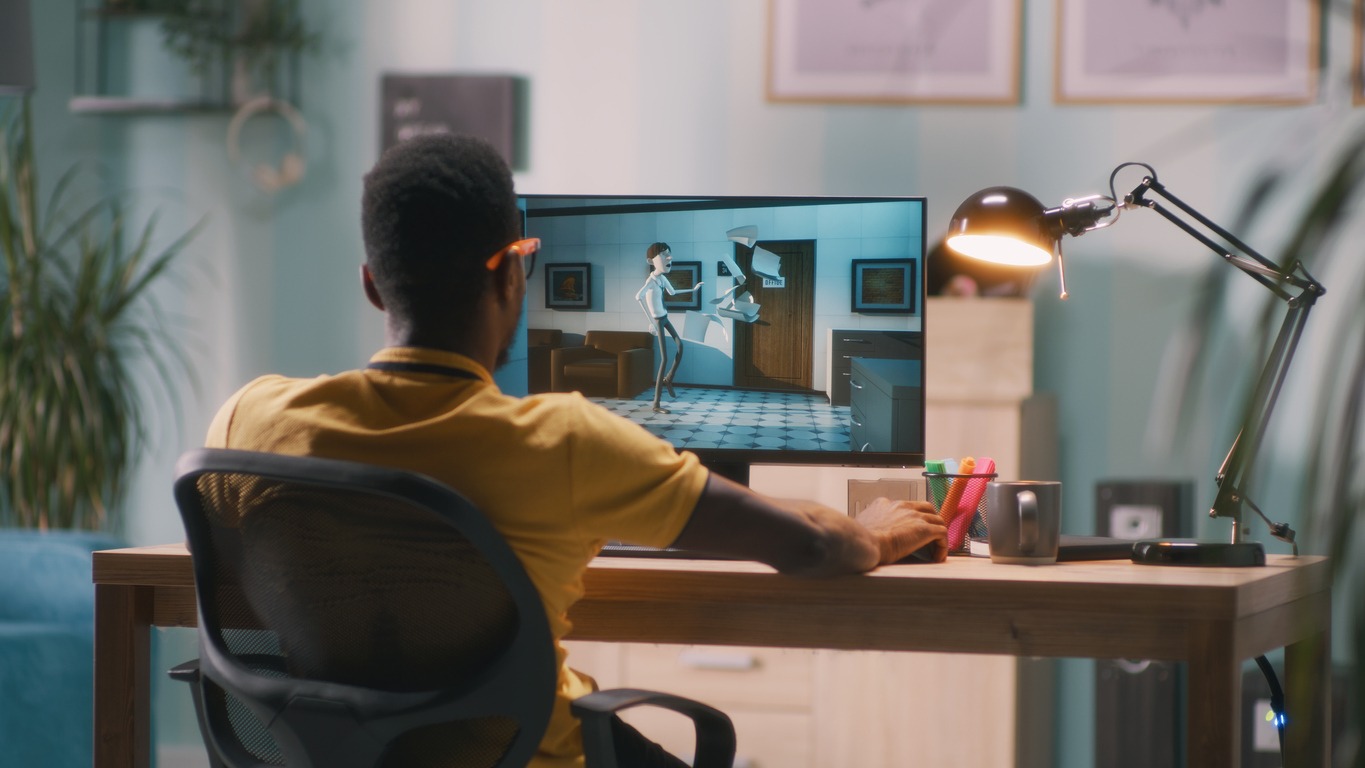Black man in glasses rendering 3D cartoon on a computer while working in home office