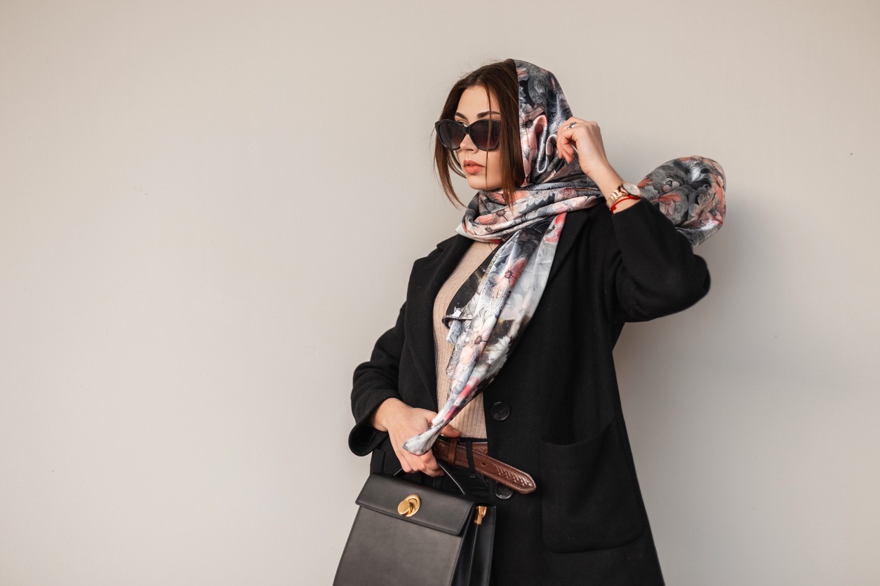 a woman in a stylish get up wearing a scarf and holding a black handbag