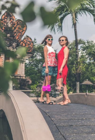 two-women-wearing-sunglasses-and-holding-bags-standing-on-foot-bridge