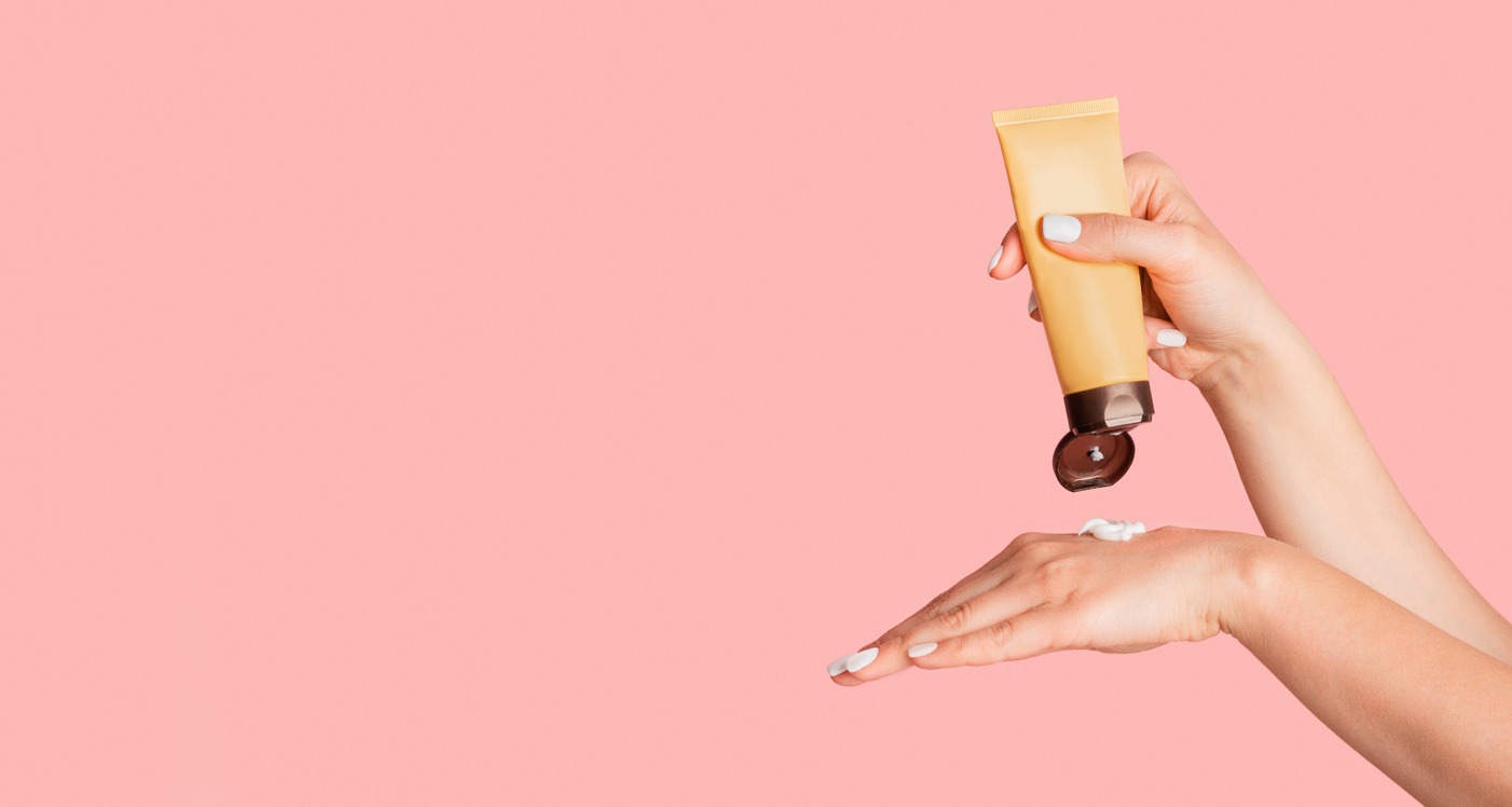 Millennial woman applying hand cream from tube over pink background, blank space. Panorama