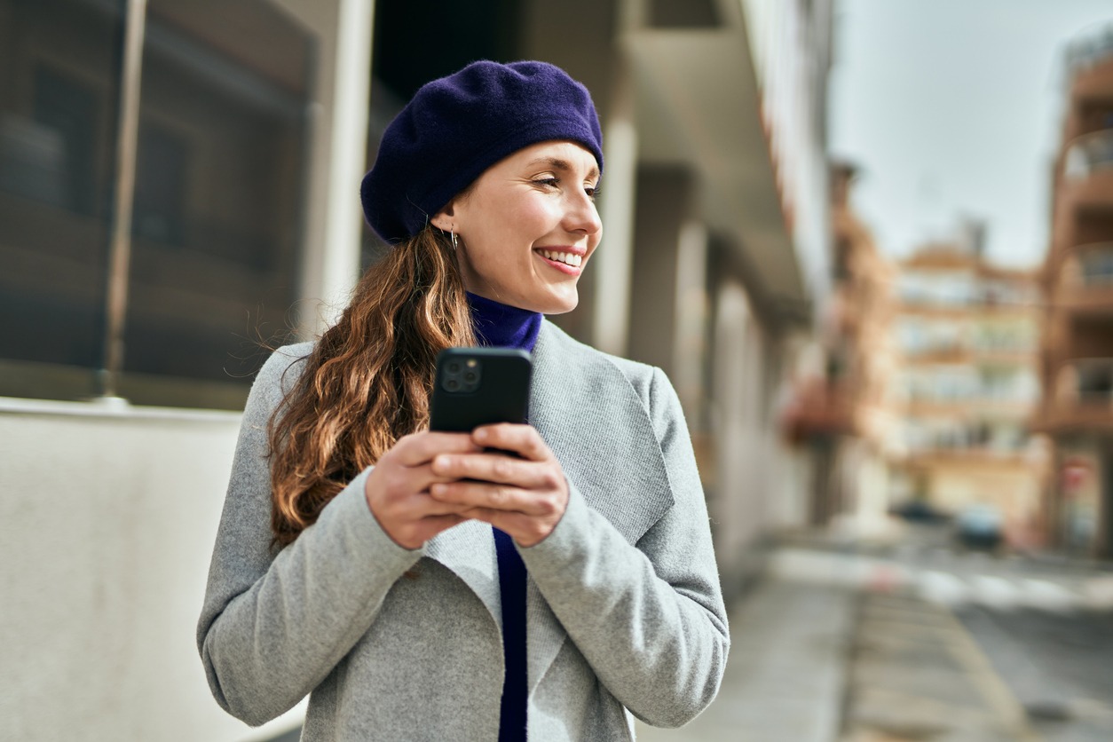 Young blonde woman smiling happily using smartphone in the city