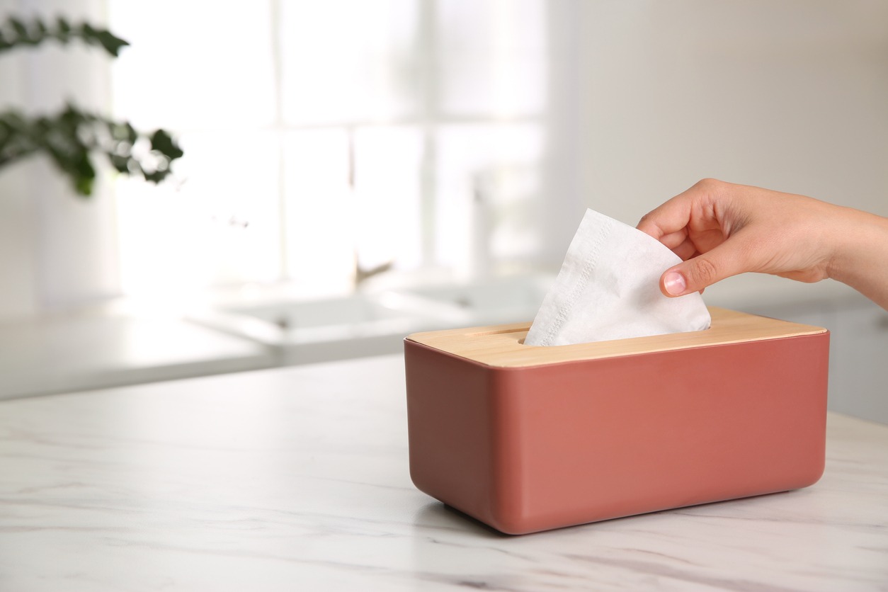 Woman taking paper tissue out of box on white marble table in kitchen, closeup