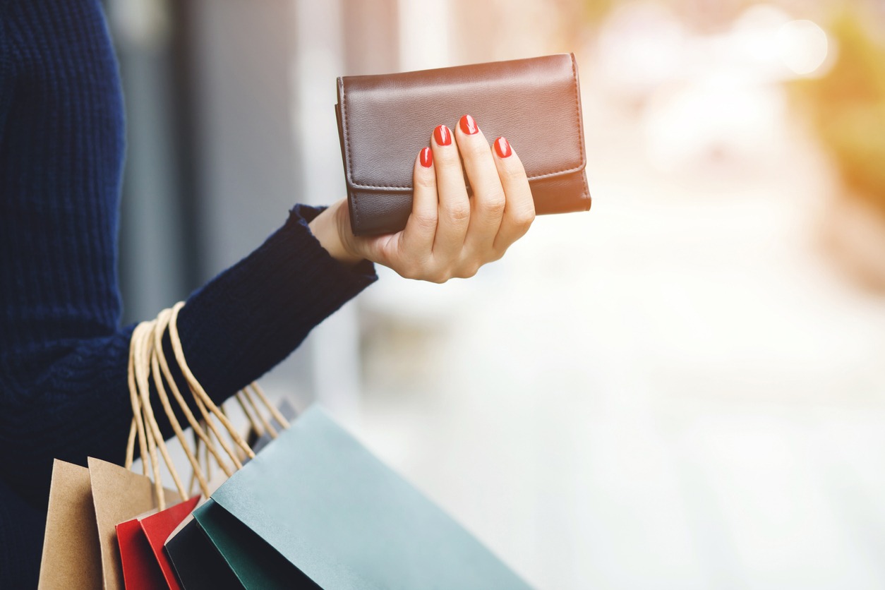 A woman holding a wallet on hand while holding shopping bags on her arms