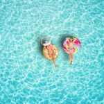 A happy vacation couple in swimsuits enjoys the tropical sun of the Maldives on colorful floats over turquoise colored sea