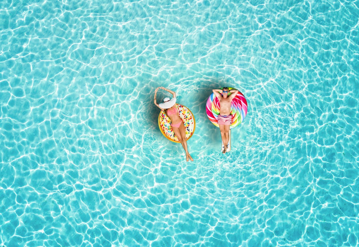 A happy vacation couple in swimsuits enjoys the tropical sun of the Maldives on colorful floats over turquoise colored sea