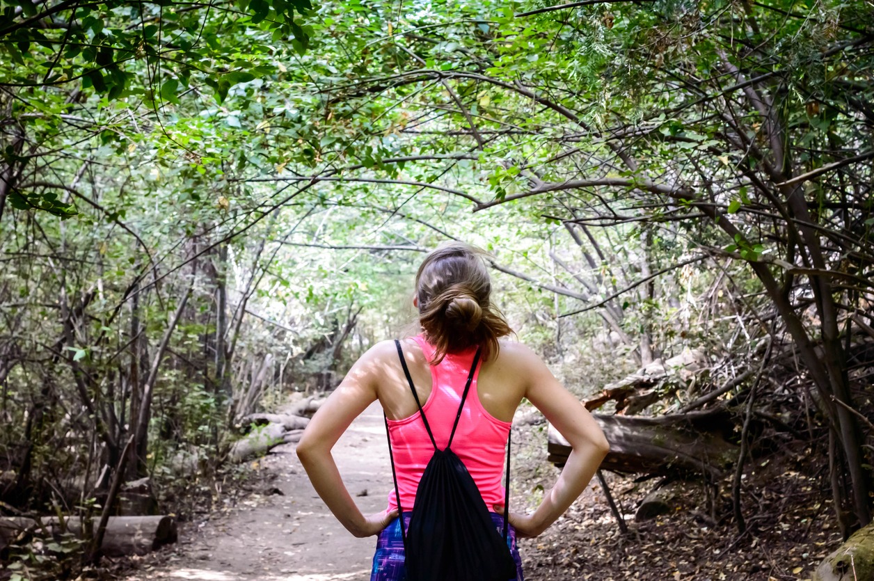 Rear view of a sexy hiker woman with a drawstring bag along the forest