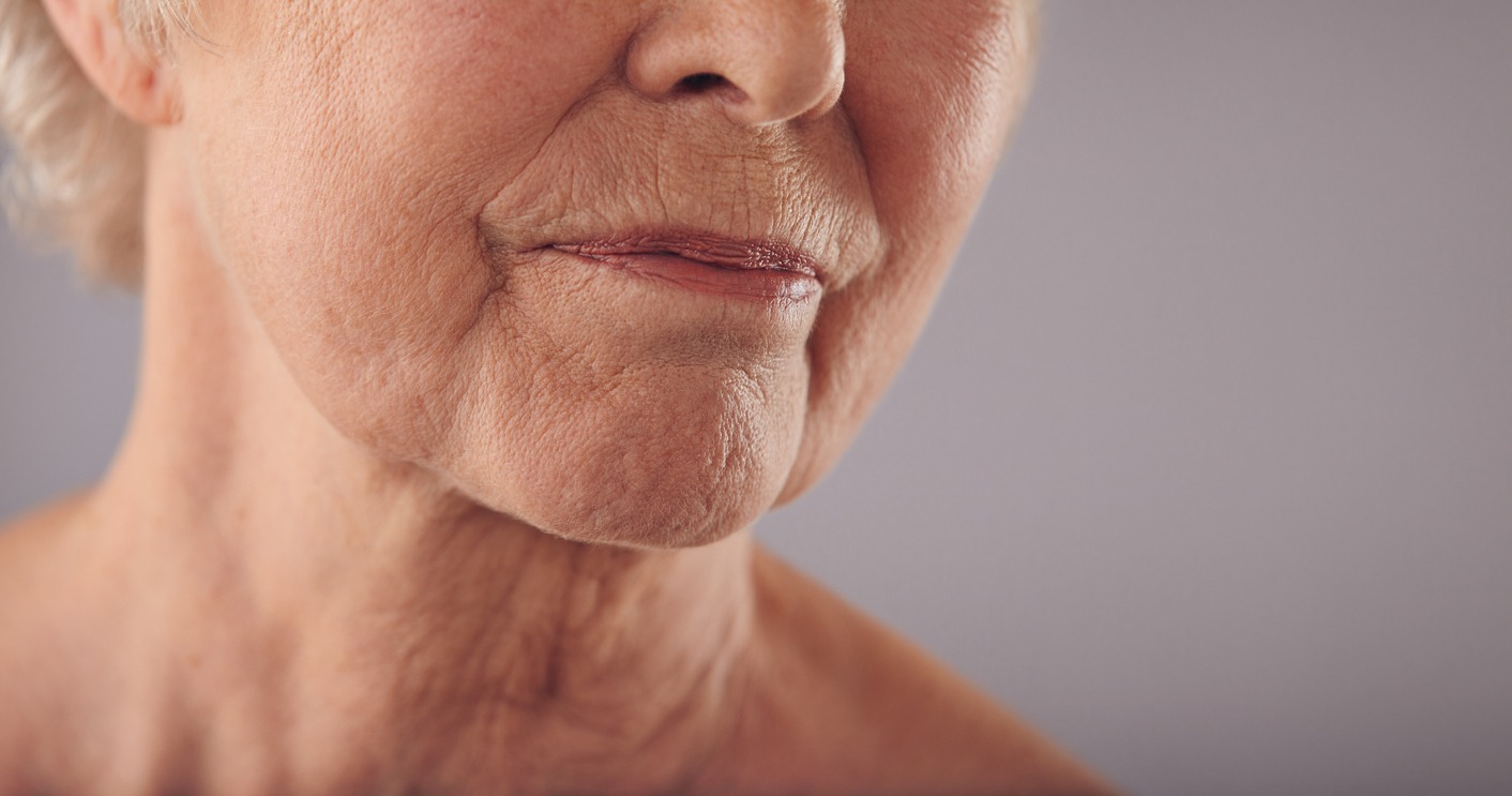 Macro of a senior female face with wrinkled skin against grey background. Cropped old woman face.