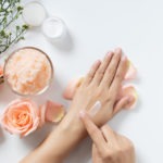 natural skincare concept. woman apply white cream on her hands on white background with jar of cosmetic cream, salt spa scrub ,rose and white flowers