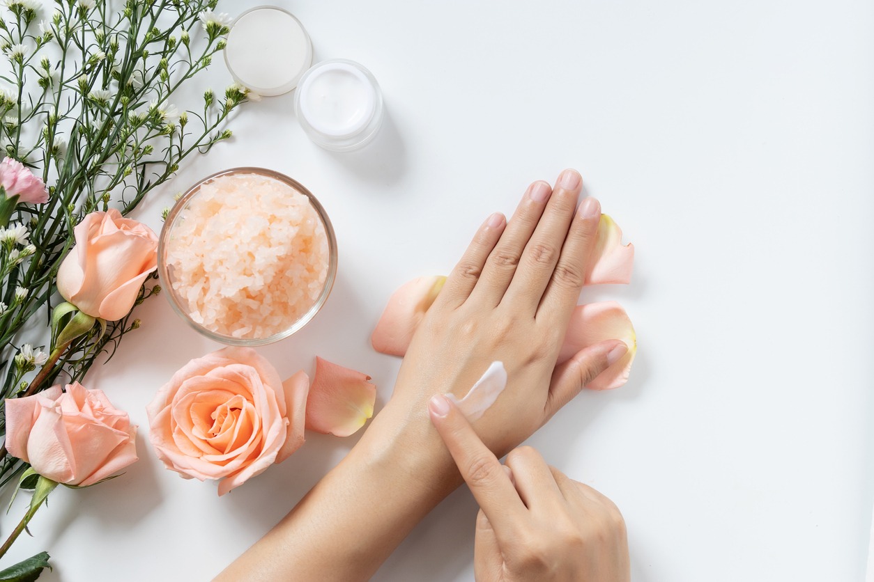 natural skincare concept. woman apply white cream on her hands on white background with jar of cosmetic cream, salt spa scrub ,rose and white flowers