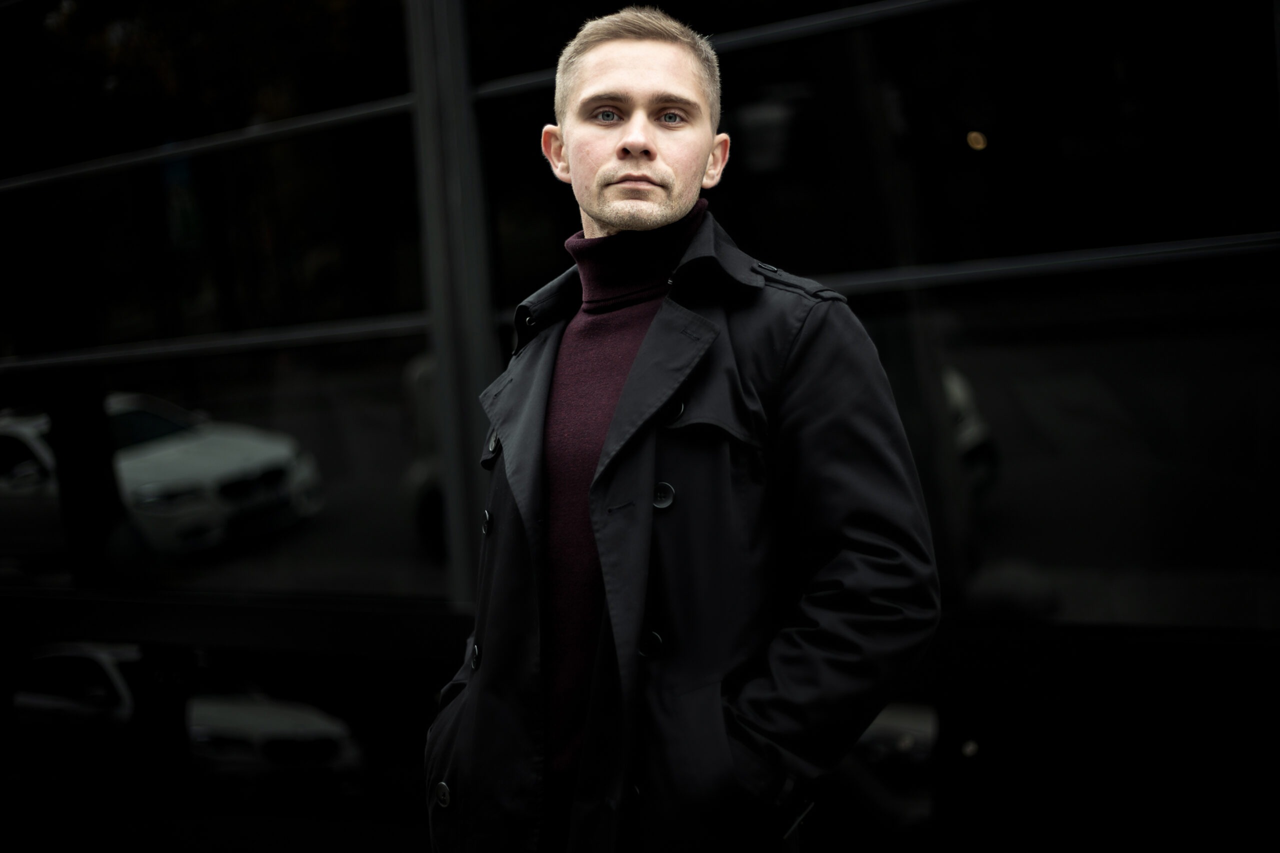 Ukrainian man in black trench coat and purple polo neck on black background