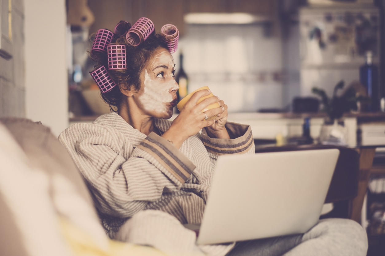 woman at home with rollers on her hair while using the laptop and sipping coffee