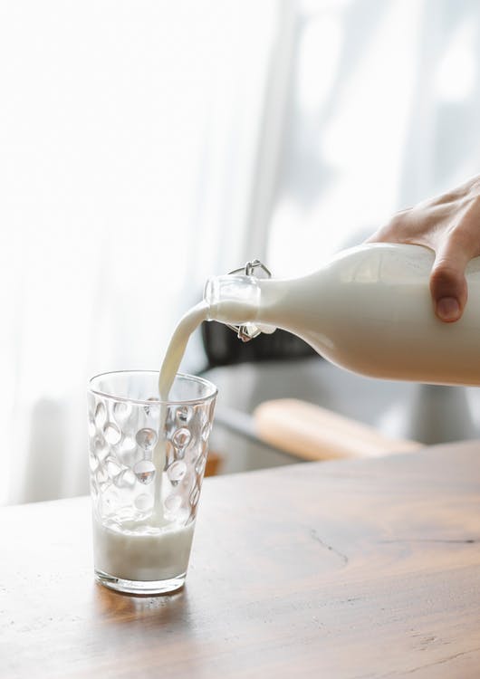 A-person-pouring-milk-from-a-glass-bottle-into-a-glass.