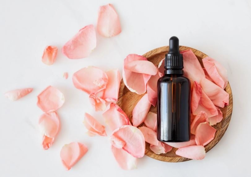 a-cosmetic-bottle-with-pink-rose-petals-on-a-wooden-plate