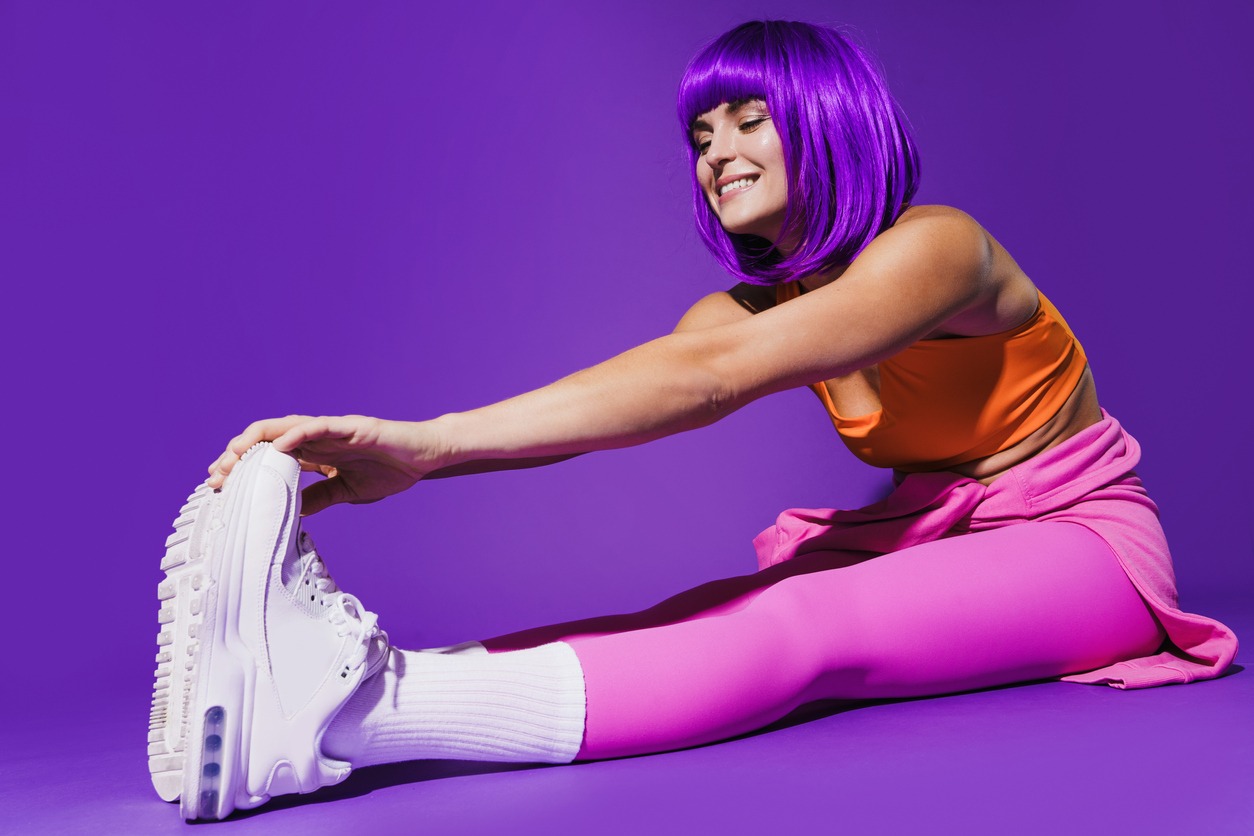 Cheerful woman wearing colorful sportswear during stretching workout against purple
