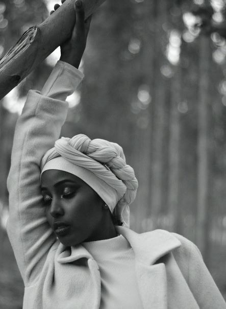 a-black-and-white-photo-of-a-woman-with-a-head-wrap-holding-a-tree-branch