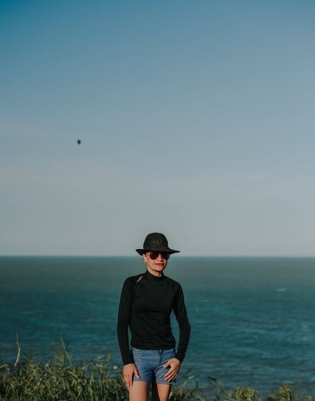 a-woman-wearing-a-hat-and-a-black-rash-guard-posing-by-the-beach