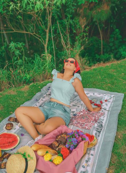 a-woman-wearing-a-head-wrap-and-sunglasses-sitting-on-a-picnic-blanket-looking-towards-the-sky