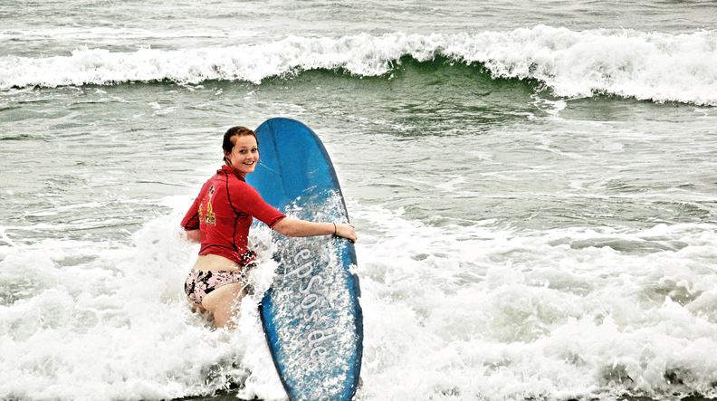 a-woman-wearing-a-rash-guard-holding-a-surf-board-against-the-waves