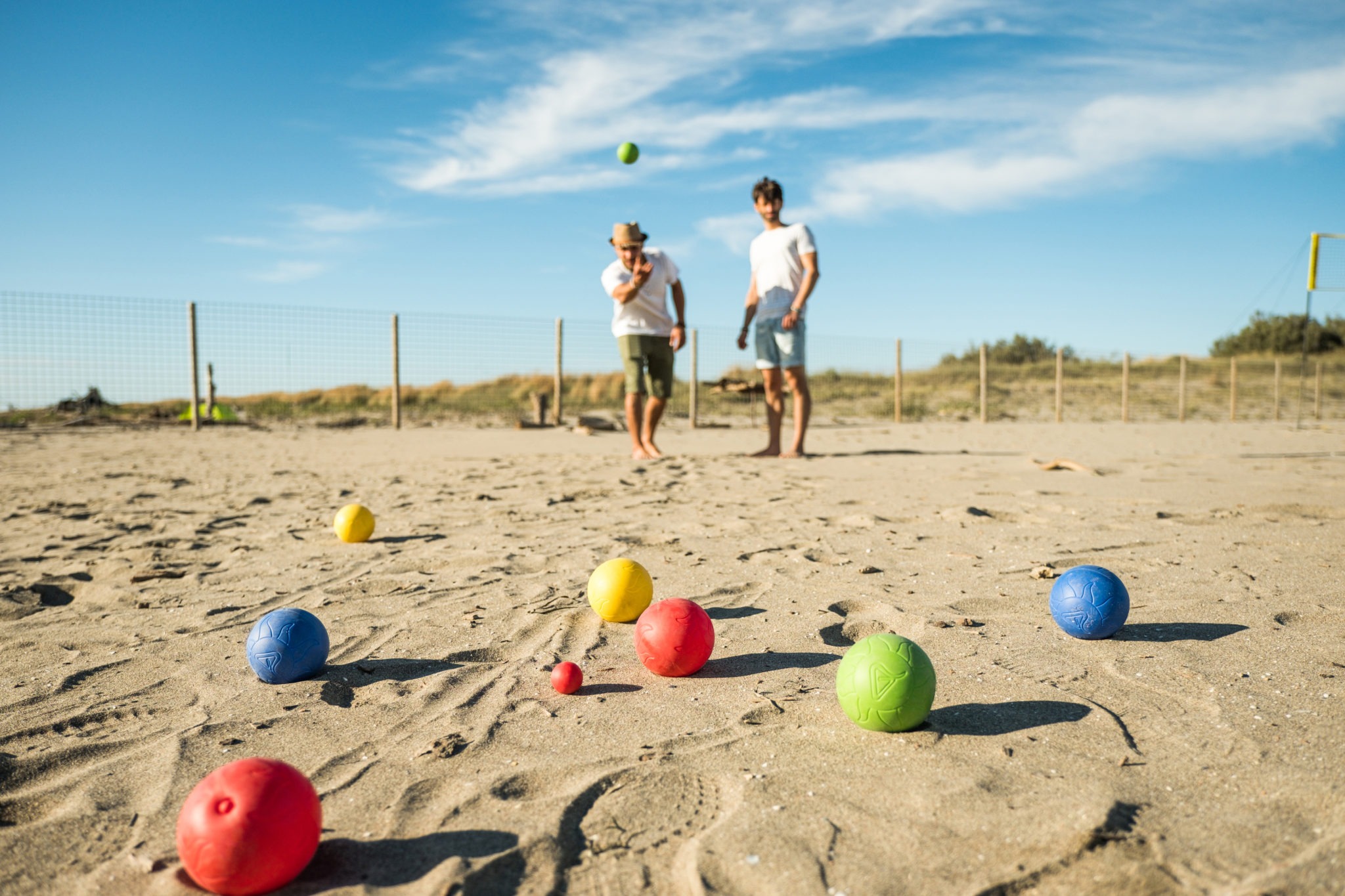 Tourists play an active game, petanque on a sandy beach by the sea - Group of young people playing boule outdoors in beach holidays - Balls on the ground