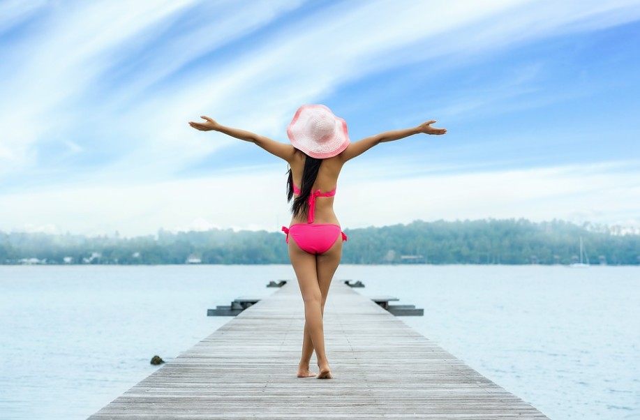 the-back-of-a-woman-wearing-a-bikini-and-a-hat-woman-spreading-her-arms-boardwalk-lake-water