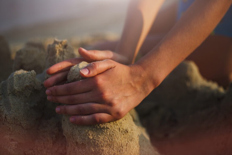 Young Caucasian woman making a sandcastle. Close-up of hands.